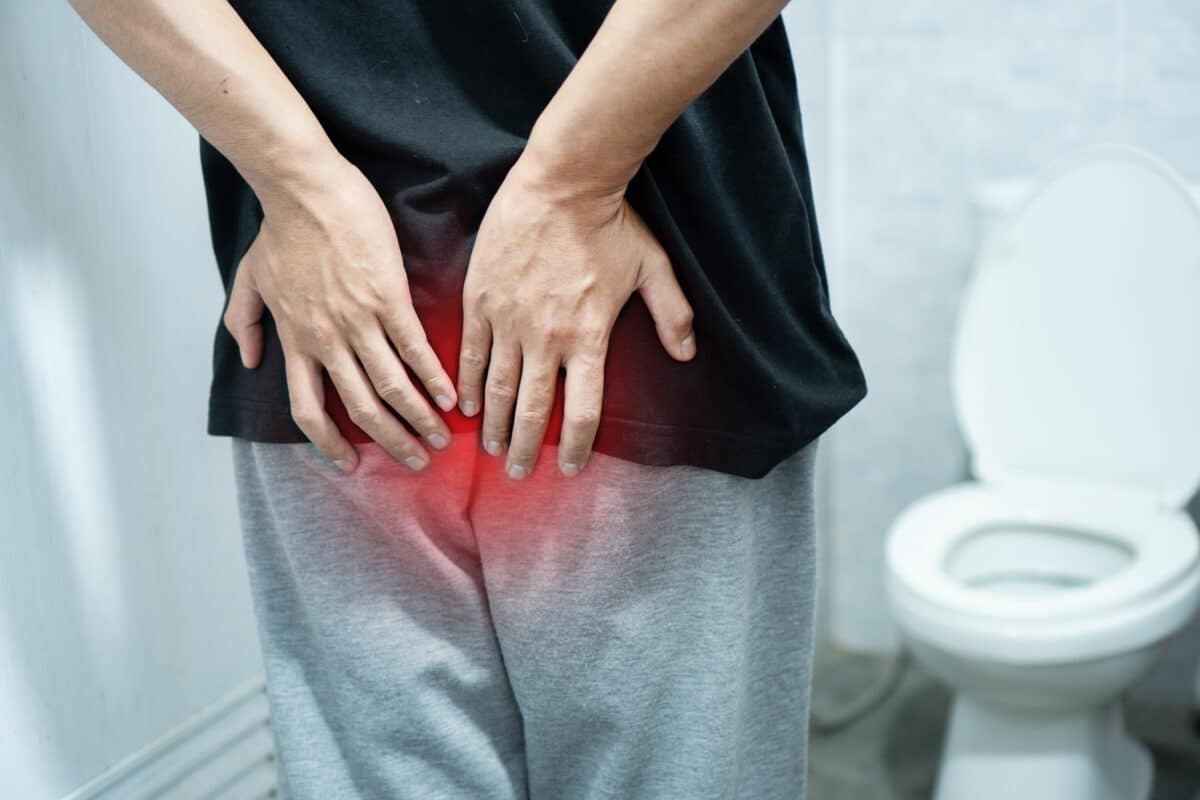 Man suffering from hemorrhoids or rectal pain holding his buttocks in bathroom. Concept of anal fissure, constipation, diarrhea, or colon cancer symptoms. Professional medical healthcare stock.