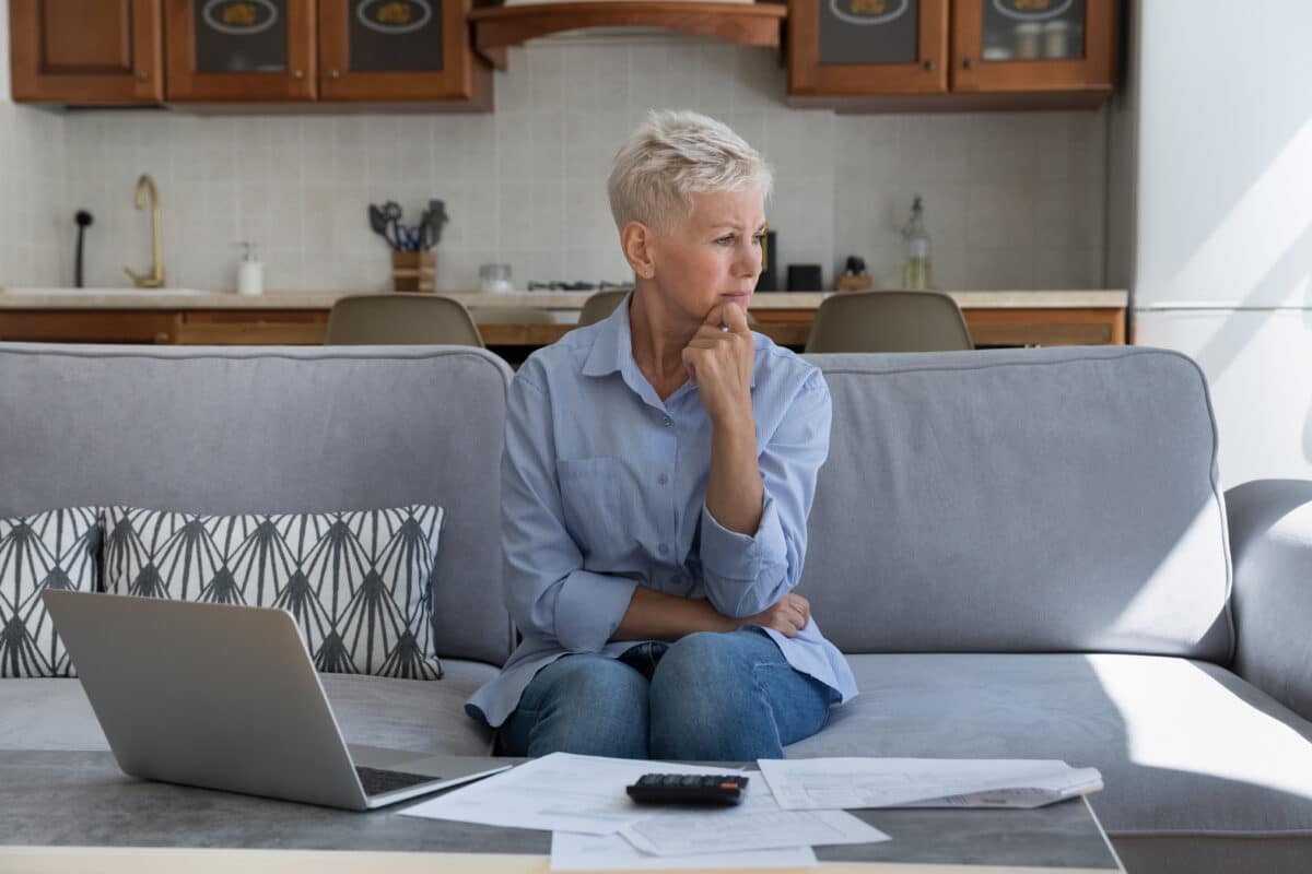 Confused old lady sit on sofa think about paying debts