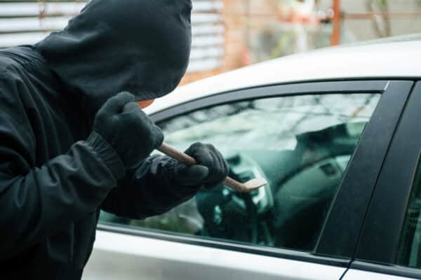 Close-up of a thief wearing balaclava breaking car window with crowbar.