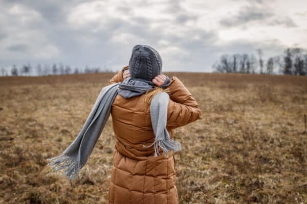 Wind and cold weather. Woman wearing coat, scarf and knit hat outdoors
