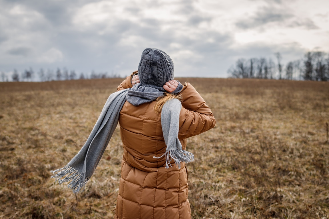 Wind and cold weather. Woman wearing coat, scarf and knit hat outdoors