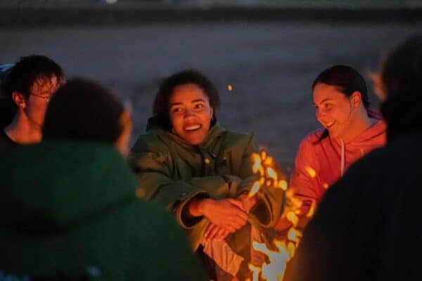Pic of a group of people sitting around a fire on a beach.