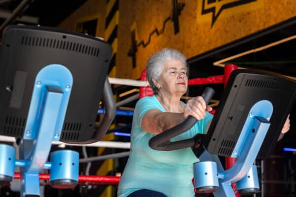 Active senior woman exercising on Stationary Bike in gym. Concept of menopause fitness, bone health, osteoporosis prevention and healthy aging. Mature woman maintaining strength and mobility