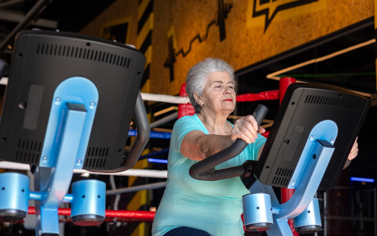Active senior woman exercising on Stationary Bike in gym. Concept of menopause fitness, bone health, osteoporosis prevention and healthy aging. Mature woman maintaining strength and mobility