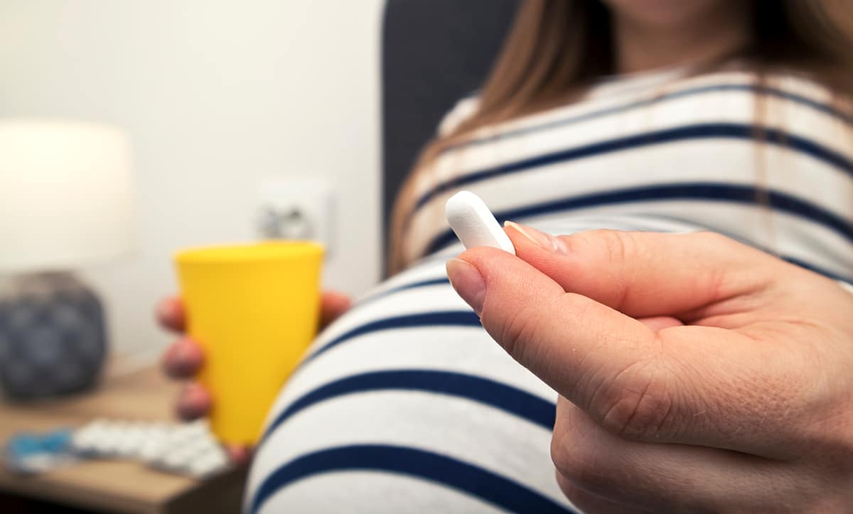 The pills in the pregnant woman’s hand sitting on the bed