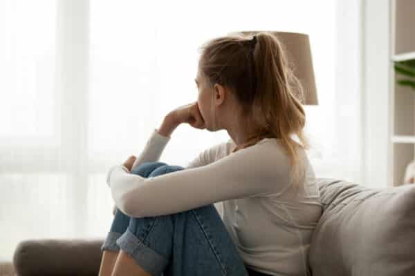 Side view young teen/woman looking away at window sitting on couch at home.