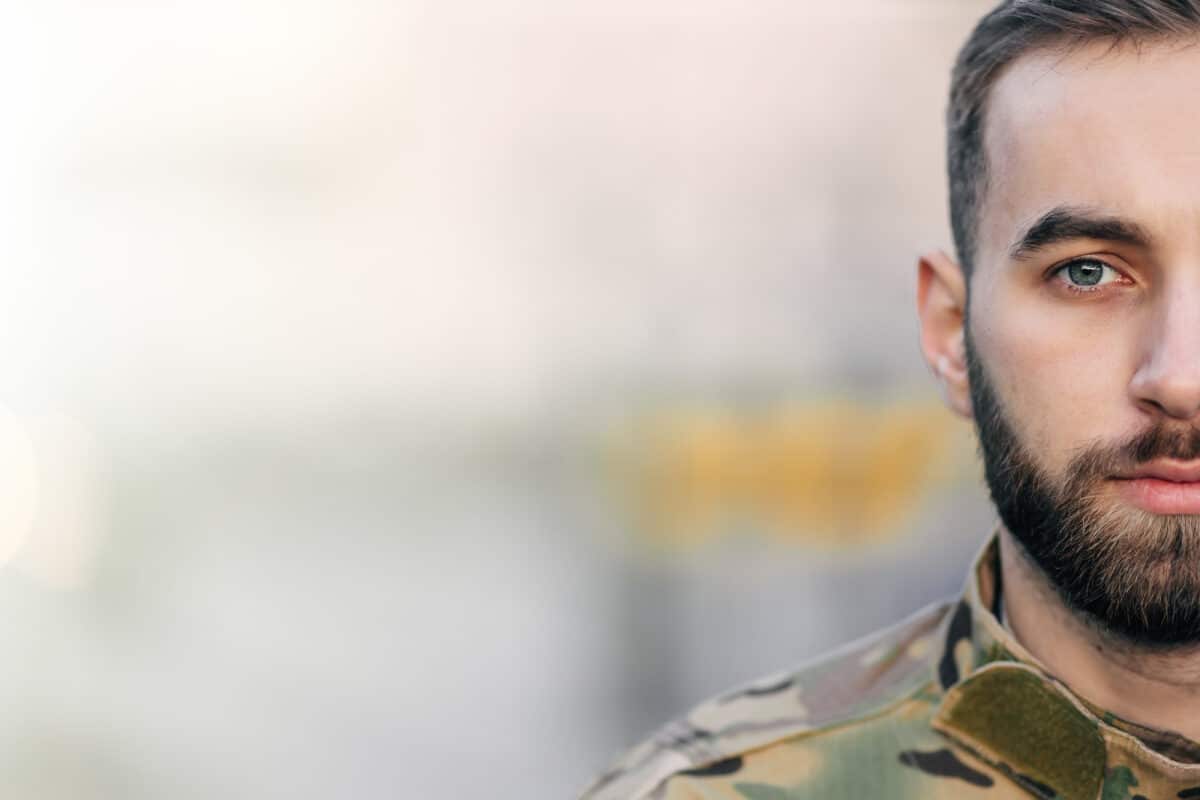 half of the face of a male soldier in camouflage uniform with a beard and sad eyes.