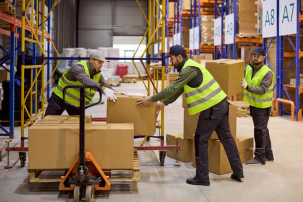 Warehouse workers loading cardboard boxes onto pallet in distribution center