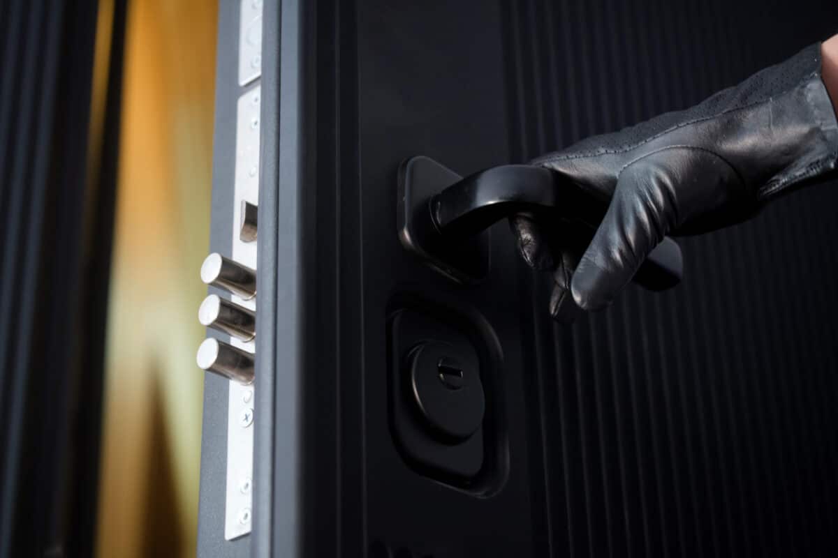 A burglar’s gloved hand opens a high-security door. Concept of housebreaking, theft, and property crime with a modern armored door lock. Photo