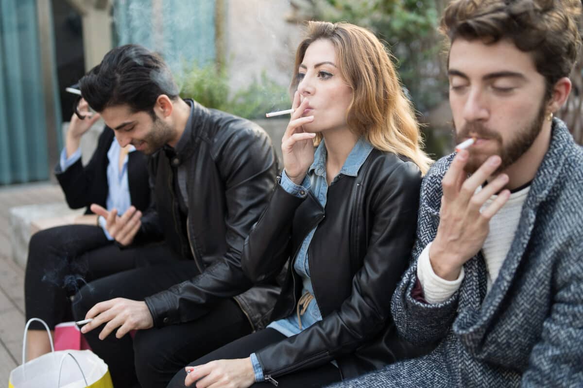 Bad habits – group of young friends smoking cigarettes together outdoors. Unhealthy addiction concept.