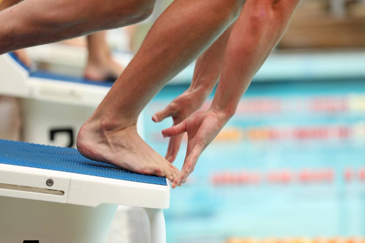 A close up view of a swimmers feet and hands on the starting blocks at the exact moment of starting a race. Foot in focus, small amount of motion blur to suggest movement.